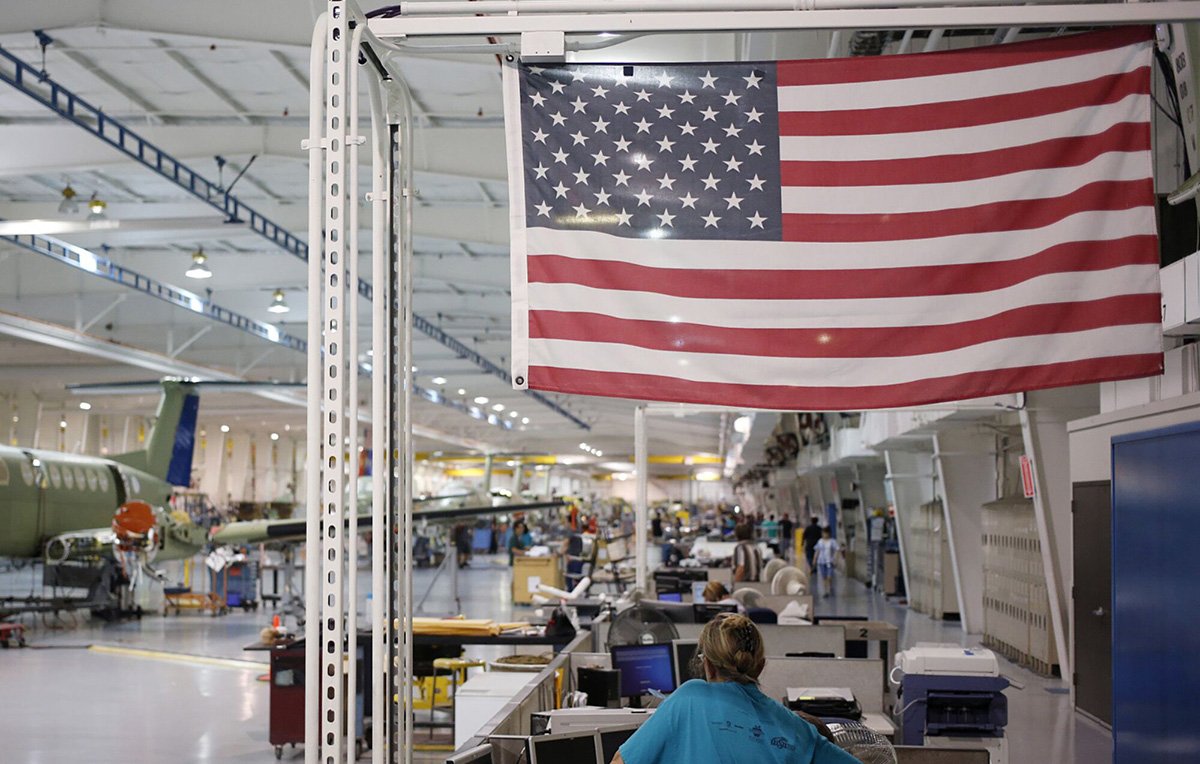 Photo: An American flag above employees at a factory in Wichita, Kansas. Photographer: Luke Sharrett/Bloomberg
